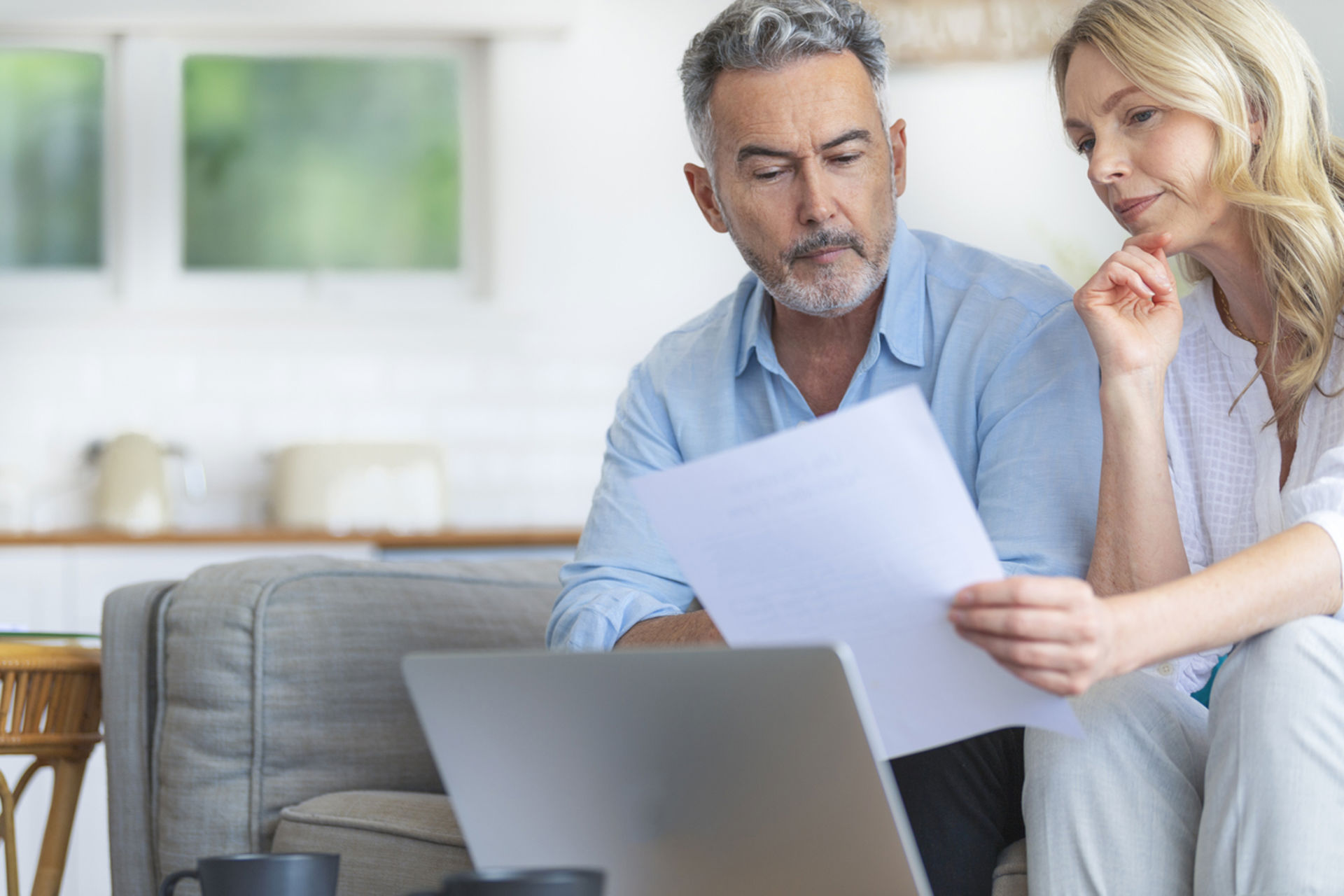 Seniorenkoppel thuis op de bank kijkend naar document en laptop